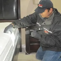 Bed bug inspection technician checking a mattress and bed frame for signs of infestation in Mesa, AZ