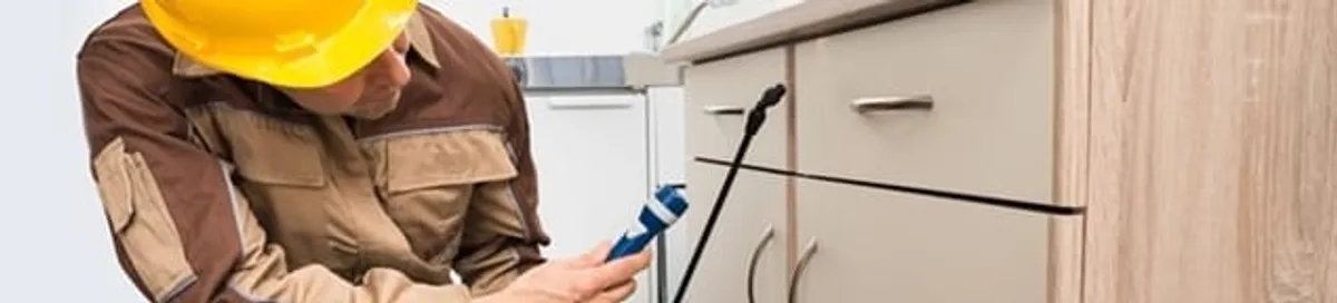 Roach exterminator applying treatment under kitchen cabinets in Mesa, AZ
