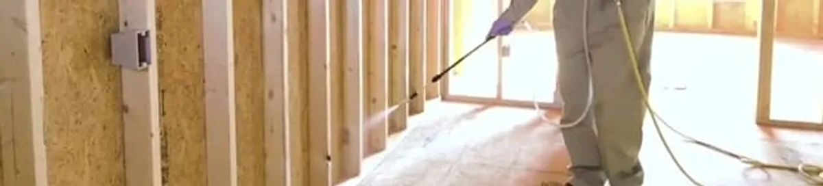Termite treatment technician applying spray along framing and unfinished walls in Mesa, AZ